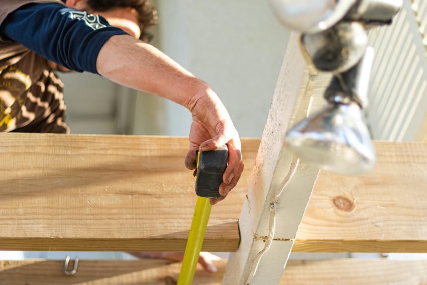builder tradie measuring a piece of timber with a yellow tape measure
